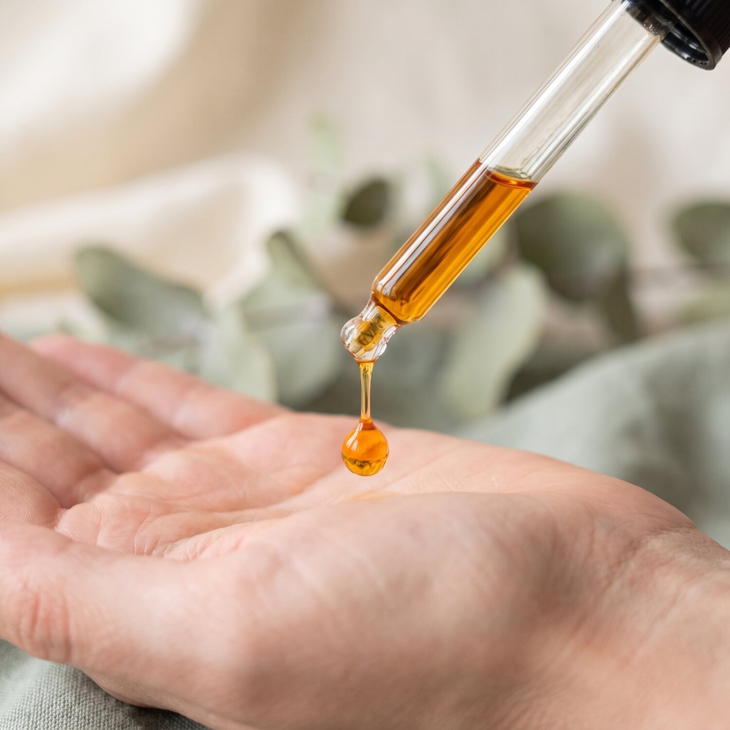 Dropper releasing a drop of golden oil onto a palm